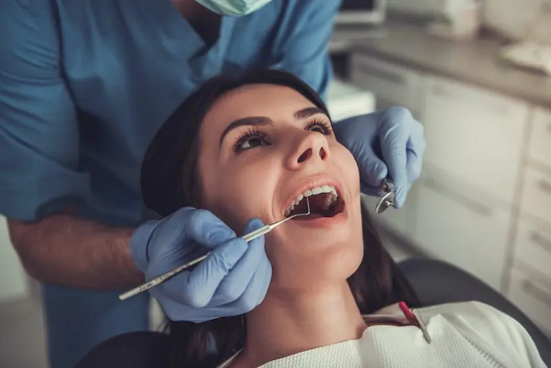 Young woman is sitting in dentist's chair while doctor is examining her teeth